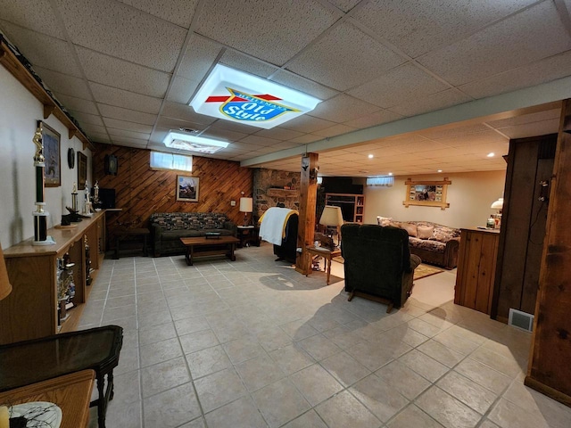 basement with a drop ceiling, visible vents, and wooden walls