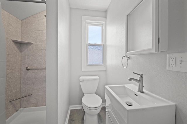 full bath featuring toilet, wood finished floors, a sink, baseboards, and tiled shower