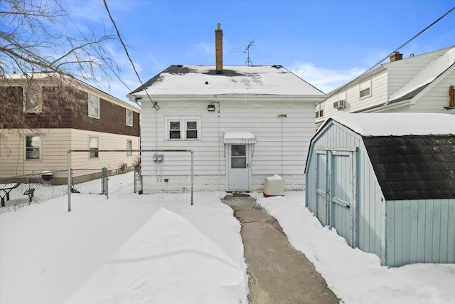 snow covered back of property featuring fence, a storage unit, and an outdoor structure