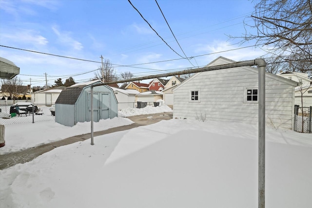 snow covered house featuring a storage unit, an outdoor structure, fence, and a residential view