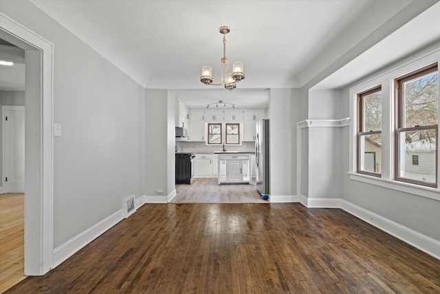 unfurnished dining area featuring an inviting chandelier, baseboards, visible vents, and wood finished floors