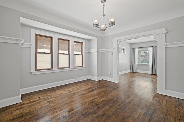 unfurnished dining area featuring a chandelier, dark wood-type flooring, and baseboards