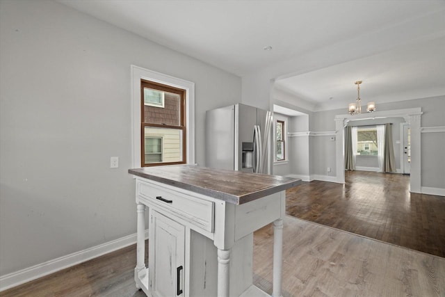 kitchen with stainless steel refrigerator with ice dispenser, hanging light fixtures, an inviting chandelier, white cabinets, and wood finished floors