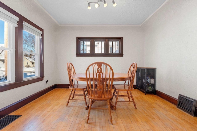 dining room with light wood finished floors, baseboards, visible vents, and crown molding