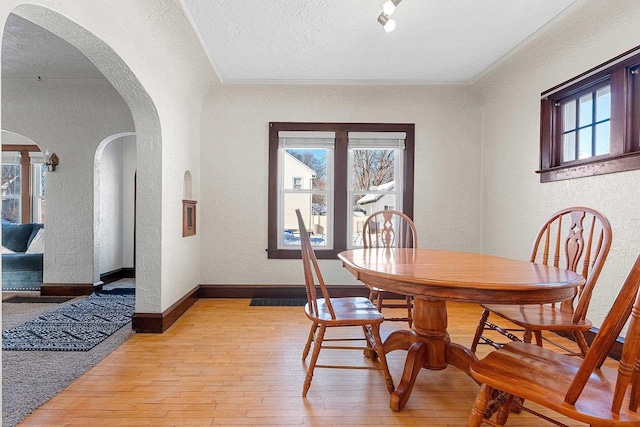 dining room with baseboards, arched walkways, a textured wall, a textured ceiling, and light wood-type flooring