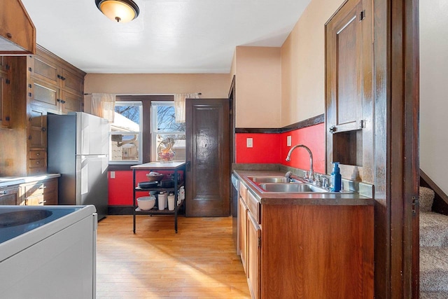 kitchen featuring brown cabinetry, freestanding refrigerator, light wood-style floors, and a sink