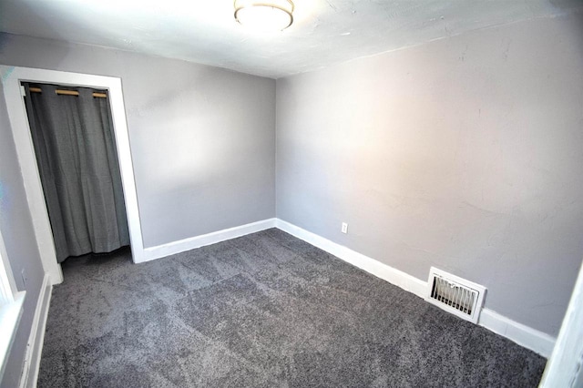 unfurnished bedroom with baseboards, visible vents, dark carpet, and a closet