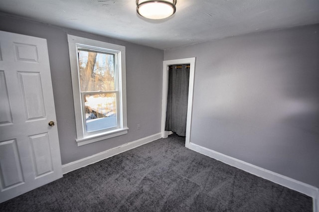 unfurnished room with baseboards and dark colored carpet