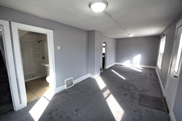 carpeted spare room featuring baseboards, visible vents, arched walkways, and a textured ceiling