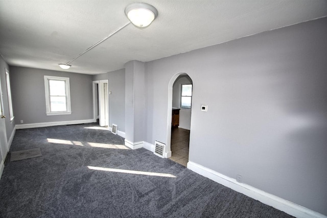 spare room with arched walkways, dark carpet, visible vents, and baseboards