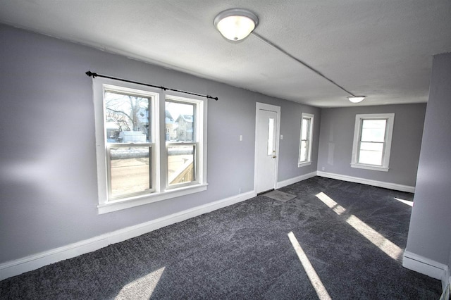 foyer featuring dark colored carpet, a textured ceiling, and baseboards