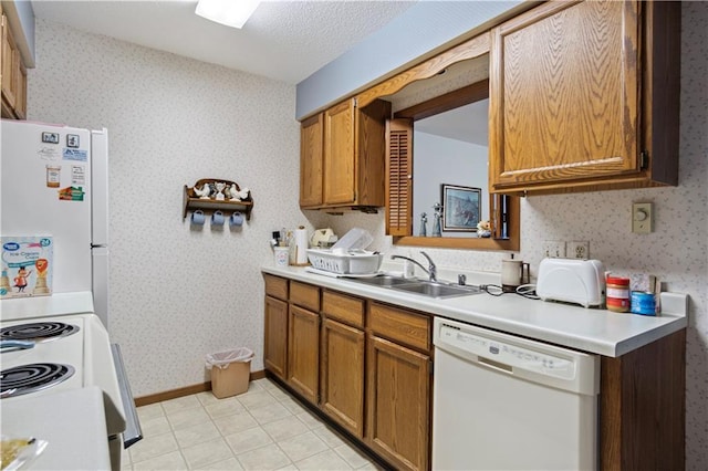 kitchen featuring white appliances, a sink, light countertops, brown cabinetry, and wallpapered walls