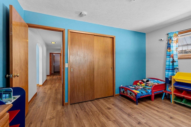 bedroom with a textured ceiling, a closet, wood finished floors, and baseboards