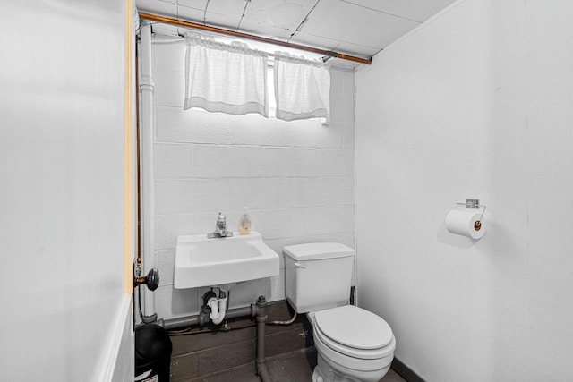 bathroom with a sink, toilet, and concrete block wall