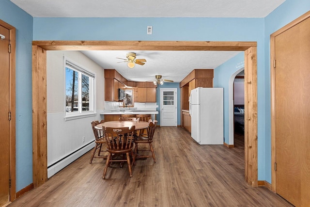 dining area featuring arched walkways, baseboard heating, ceiling fan, a textured ceiling, and light wood-type flooring