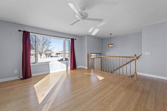 spare room with light wood-type flooring, baseboards, and ceiling fan with notable chandelier