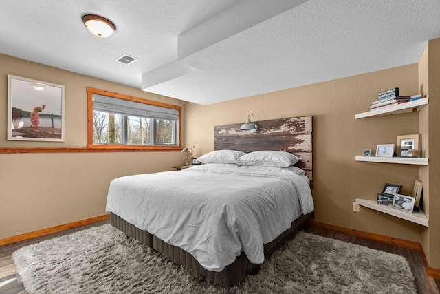 bedroom with visible vents, a textured ceiling, baseboards, and wood finished floors