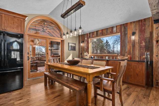 dining room with lofted ceiling, wood walls, wood finished floors, and a textured ceiling