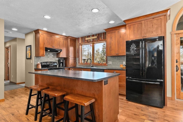 kitchen with under cabinet range hood, a sink, a center island, black appliances, and dark countertops