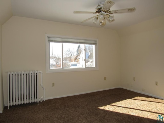 empty room featuring lofted ceiling, dark colored carpet, radiator heating unit, and a ceiling fan