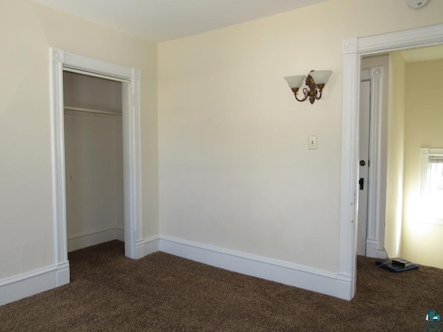 unfurnished bedroom with a closet, dark carpet, and baseboards