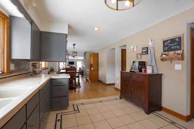 kitchen featuring decorative light fixtures, light tile patterned floors, light countertops, a peninsula, and baseboards