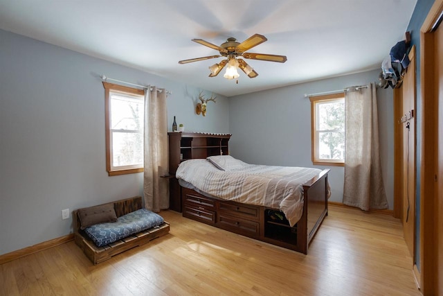 bedroom featuring ceiling fan, multiple windows, baseboards, and light wood-style floors