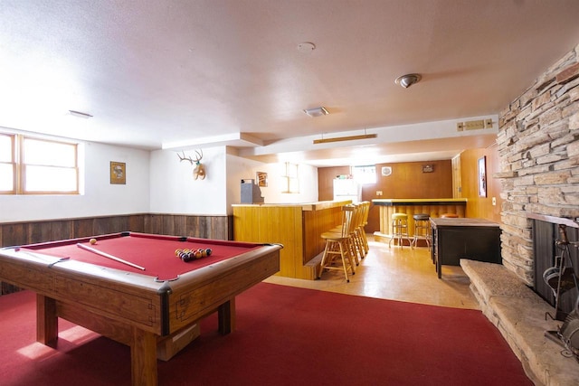 recreation room featuring wooden walls, visible vents, wainscoting, a bar, and a fireplace