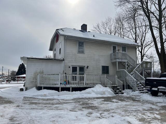 snow covered rear of property with stairs, a chimney, and a deck