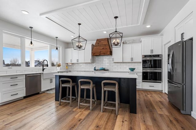 kitchen with appliances with stainless steel finishes, custom range hood, a kitchen island, and white cabinetry