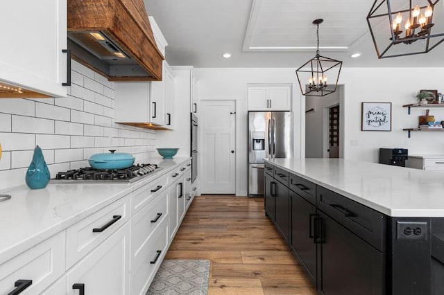 kitchen featuring decorative light fixtures, custom exhaust hood, stainless steel appliances, light countertops, and white cabinetry