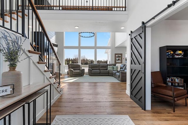 living room with stairs, a barn door, light wood-type flooring, and a high ceiling