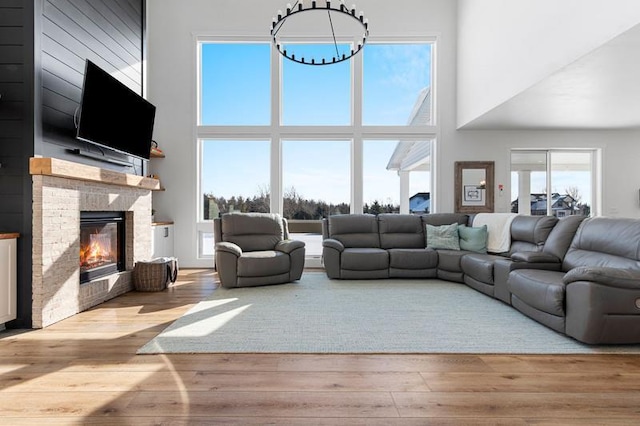 living room with a towering ceiling, light wood-style floors, a fireplace, and an inviting chandelier