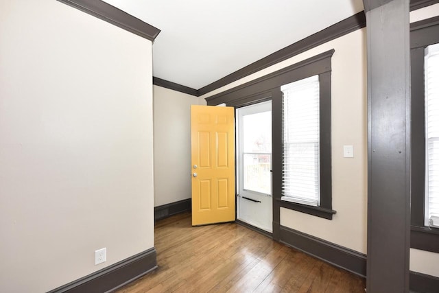 empty room with ornamental molding, light wood-style floors, and baseboards