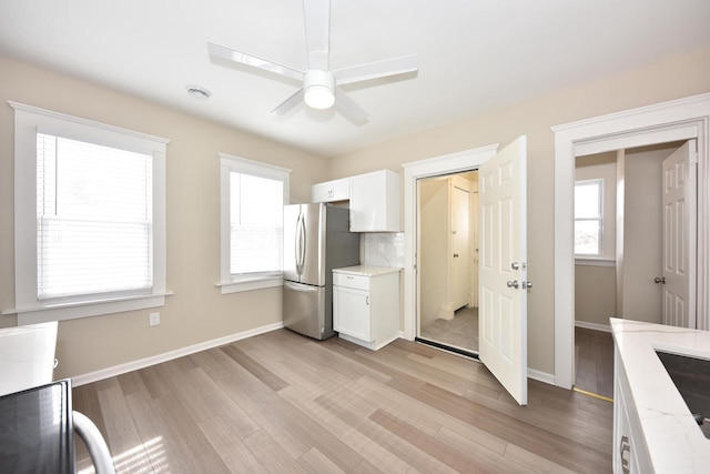 kitchen featuring baseboards, light wood finished floors, freestanding refrigerator, and white cabinets