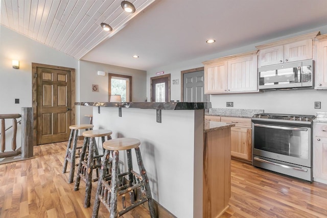 kitchen with light wood-style flooring, appliances with stainless steel finishes, a kitchen breakfast bar, vaulted ceiling, and light brown cabinets