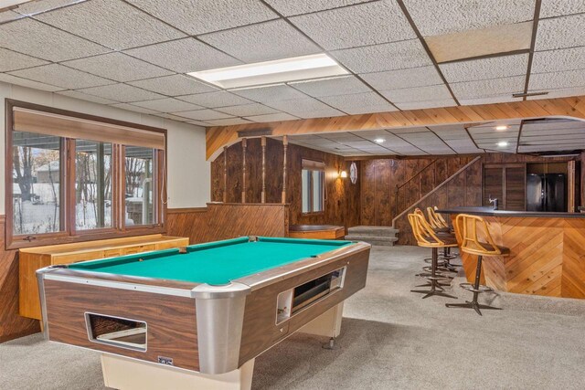 recreation room featuring a paneled ceiling, light colored carpet, pool table, wood walls, and a bar