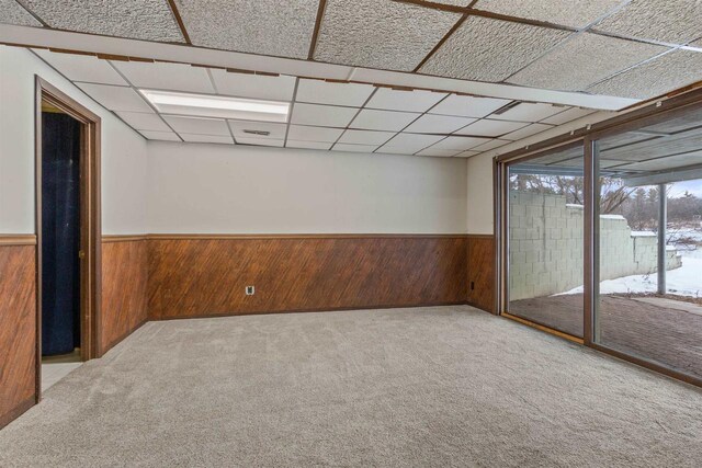 spare room with a wainscoted wall, a drop ceiling, carpet, and wooden walls