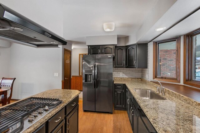 kitchen featuring stainless steel appliances, a sink, wall chimney exhaust hood, and light stone countertops