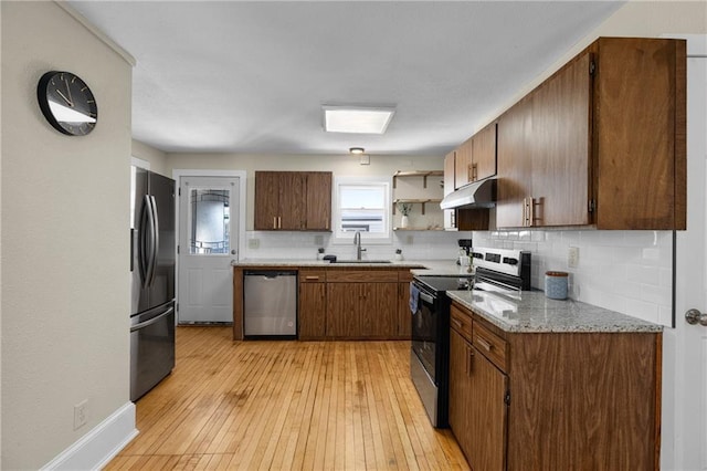 kitchen with tasteful backsplash, appliances with stainless steel finishes, a sink, light wood-type flooring, and under cabinet range hood