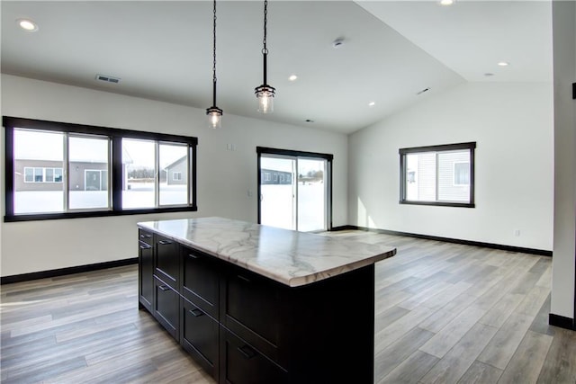 kitchen with visible vents, light wood-style flooring, a kitchen island, decorative light fixtures, and light stone countertops