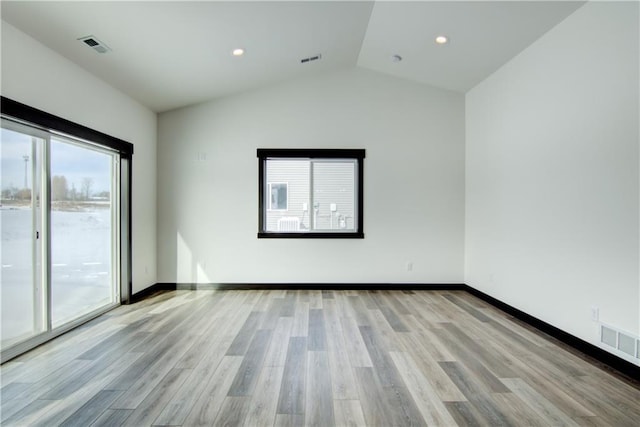 empty room with vaulted ceiling, light wood finished floors, visible vents, and baseboards