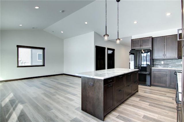 kitchen featuring a center island, decorative light fixtures, freestanding refrigerator, dark brown cabinets, and light stone countertops