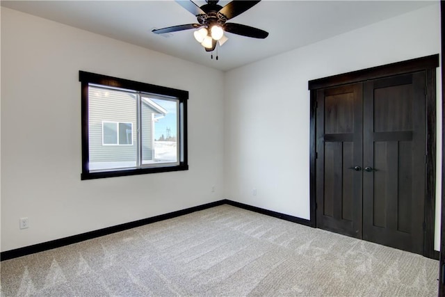 unfurnished bedroom featuring light carpet, a closet, a ceiling fan, and baseboards