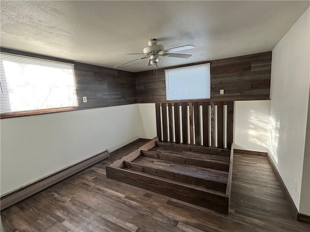 stairs with baseboard heating, ceiling fan, a textured ceiling, wooden walls, and wood finished floors