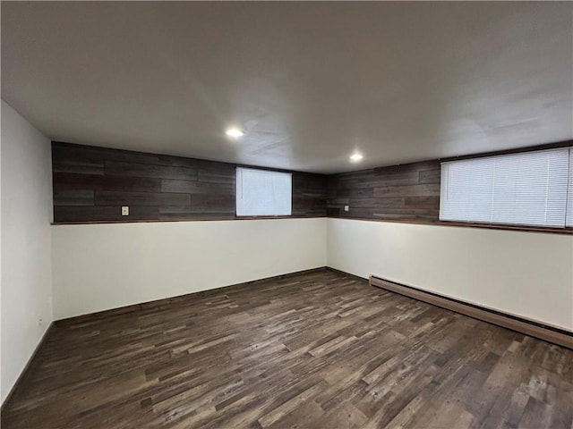 basement with dark wood-style flooring, wooden walls, a baseboard radiator, and recessed lighting
