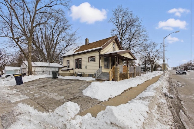 snow covered property featuring a porch and a chimney