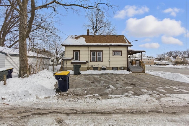 snow covered house with covered porch and a chimney