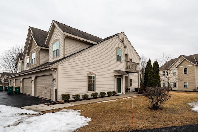 view of snowy exterior featuring a garage, driveway, and a balcony