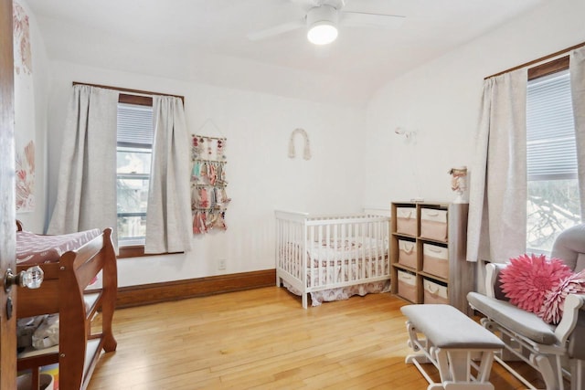 bedroom featuring a ceiling fan, multiple windows, baseboards, and wood finished floors